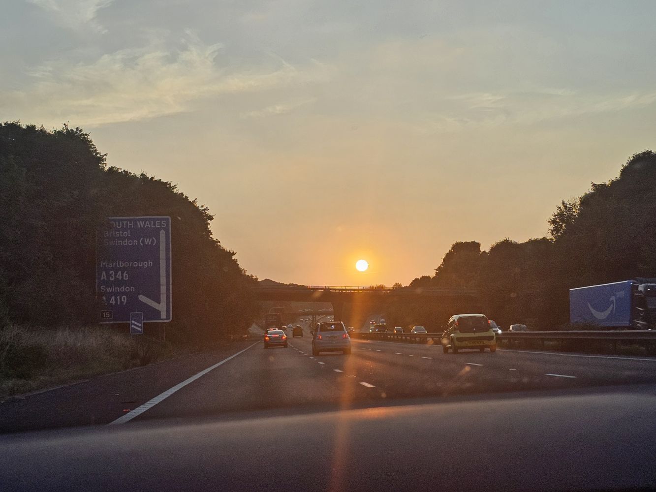 A picture of a beautiful golden sunset over the motorway as photographed from inside a car.