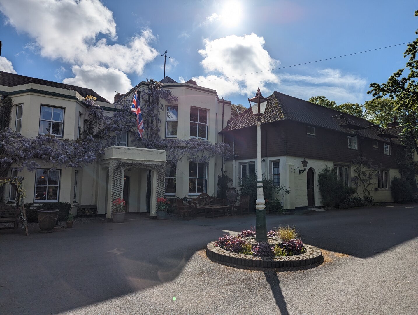 an old looking English country house with purple wisteria growing around it and the sun shining